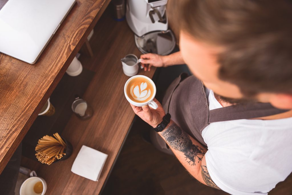 cup of coffee art with the shape of heart in hands of cafe worker, high angle