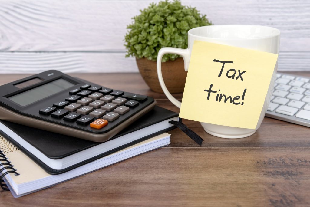 Tax time text written on sticky note with calculator on top of desk - business and financial concept