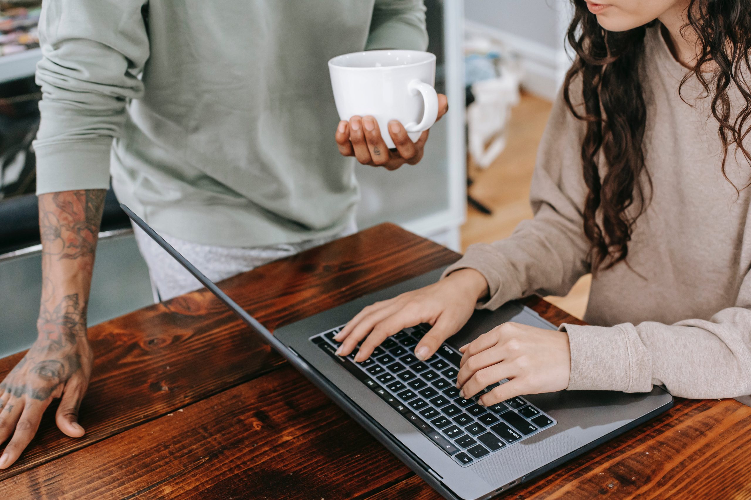 accountant working on a table while her partner is holding a coffee