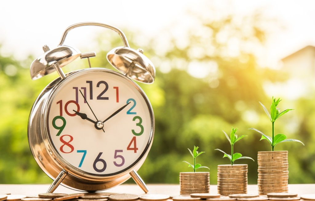 large clock beside stack of coins that is growing