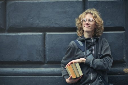 accountant student holding books while leaning on a wall