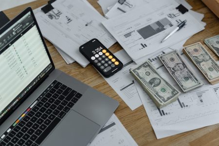 money calculator laptop and papers on top a wooden desk