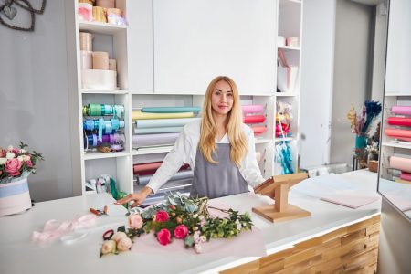 Beautiful blonde lady in an apron posing at the counter of a flower shop