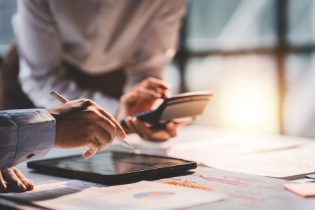 Young colleagues discuss business and analytical price charts using calculators and laptops to calculate financial, tax, accounting, statistics and analytical research ideas.